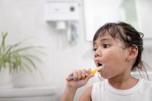 liten söt flicka som rengör sina tänder med en tandborste i badrummet foto