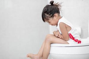 den lilla flickan sitter på toaletten och lider av förstoppning eller hemorrojder. foto