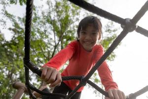 sommar, barndom, fritid och människor koncept - glad liten flicka på barnens lekplats klättringsram foto