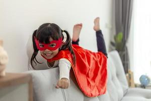 barn flicka i en superhjälte kostym med mask och röd kappa hemma foto