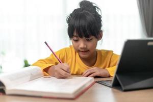 Asiatisk liten flicka tar klass på nätet och glad för homeschool karantän coranavirus pandemi koncept foto