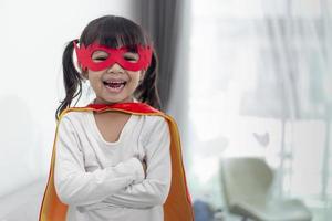 barn flicka i en superhjälte kostym med mask och röd kappa hemma foto