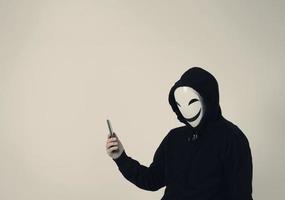 anonym hacker och ansiktsmask med smartphone i handen. foto