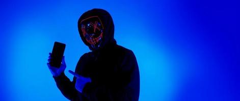 anonym hacker och ansiktsmask med smartphone i handen. foto
