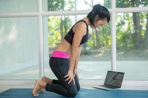 kvinna utövar yoga, tränar uppåtriktad maglås, uddiyana bandha-pose, tränar, bär sportkläder, tittar på träningsvideohandledning online på bärbar dator, tränar hemma sittande. foto