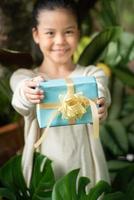 jul porträtt av glada leende liten flicka barn med presentförpackning nära en grön gren träd. foto