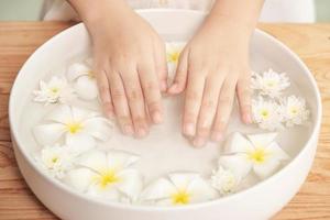 spabehandling och produkt för kvinnliga fötter och handspa. vita blommor i keramisk skål med vatten för aromterapi på spa. foto