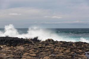 turbulenta havsvågor med vitt skum slår kuststenar foto
