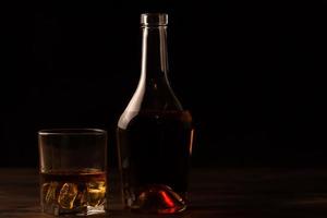 glas whisky med is och ett flaskträbord. foto