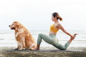 banner storlek foto, en asiatisk ung kvinna kysser sin hund på en yogamatta på stranden. avkoppling med ett husdjur. foto