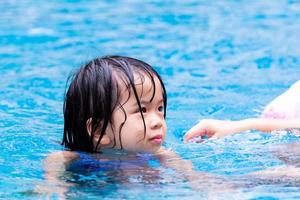 porträtt söt asiatisk barn flicka spelar i klarblå pool. barn tycker om att träna i vatten. barn 4 år gammal är blöt. foto
