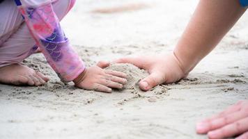 närbild dotter och fars händer gör högar av sand på stranden vid havet. glad familjesemester aktiviteter koncept. tomt utrymme för att skriva in text. foto