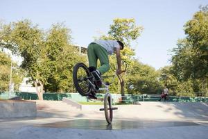 bmx ryttare tränar och gör tricks i street plaza, cykel stunt ryttare i cocncrete skatepark foto