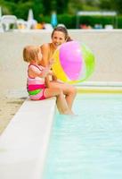 mamma och baby flicka med strandboll vid poolen foto