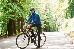 poserar för en kamera. cyklist på en cykel är på asfaltvägen i skogen på en solig dag foto