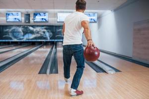 endast en person. bakifrån av mannen i fritidskläder som spelar bowling i klubben foto