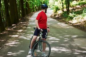 tittar bakom. cyklist på en cykel är på asfaltvägen i skogen på en solig dag foto