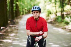 porträtt av skäggig man. cyklist på en cykel är på asfaltvägen i skogen på en solig dag foto