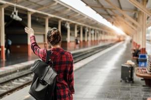 ung asiatisk kvinna backpacker resenär gå ensam på järnvägsstationen plattform med ryggsäck. asiatisk kvinna väntar tåg på tågstationen för resor. sommar semester resor eller unga turist koncept foto