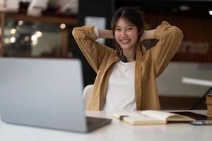 porträtt av ung asiatisk kvinna som använder bärbar dator och skriver att göra lista med anteckningar i anteckningsblock som arbetar eller lär sig på bärbar dator inomhus - utbildningskurs eller utbildning, seminarium, utbildning online-koncept. foto