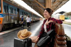 ung asiatisk kvinna resenär ryggsäck väntar järnväg på järnvägsstationen, sommarsemester och resor koncept foto
