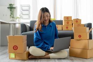 startup SM småföretagare, håller kortlåda stående på hennes hemmakontor. vacker framgång asiatisk affärskvinna onlinemarknadsföring, sme förbereder paketleverans till sin kund foto