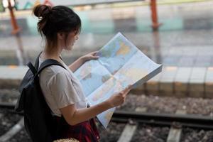en ung kvinna resenär stående med karta väljer vart att resa och väska väntar på tåget på tågstationen foto