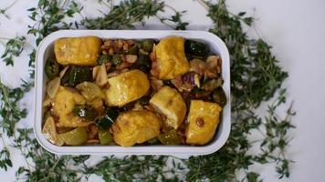 vegetabilisk tofu med gula kryddor indonesisk mat serverad i en aluminiumhållare med en vit bakgrund med några gröna blad runt omkring foto