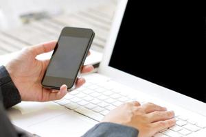 smartphone i affärskvinnas händer över en vit bärbar dator.