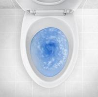 ovanifrån av toalettskålen, blått tvättmedel som spolar i den foto