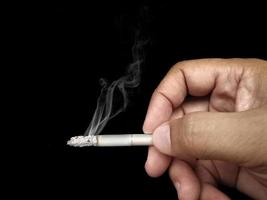 närbild en mans hand som håller en skrynklig, rykande cigarett med rök hand som röker cigarett, ohälsosamt livsstilskoncept foto