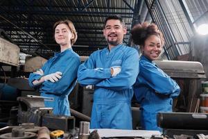 multiracial industriarbetare i säkerhetsuniformer samarbetar med enighet, armarna i kors och uttrycker lyckligt arbete tillsammans med leende och glada i mekanisk fabrik, professionell ingenjörsyrke. foto