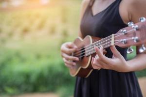 vacker kvinna som håller en gitarr på axeln, naturpark sommar utanför. foto