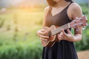 vacker kvinna som håller en gitarr på axeln, naturpark sommar utanför. foto