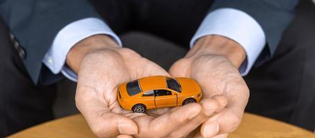 affärsman hand som håller orange bil leksak på bordet. finansiella, pengar, refinansiera och bilförsäkring koncept foto