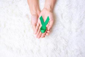 hand som håller grönt band för att stödja människor som lever och sjukdom. lever, gallblåsor gallgång, njurcancer och lymfom medvetenhet månad koncept foto
