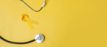 gult band och stetoskop på gul bakgrund för att stödja människor som lever och sjukdom. september självmordsförebyggande dag, barndomens cancermedvetenhetsmånad och världscancerdagens koncept foto