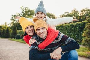 horisontella porträtt av familjemedlemmar tillbringar ledig tid tillsammans, omfamna, uppmuntra varandra, ha kul. liten leende flicka känner lycka, omfamna hennes tillgivna föräldrar. aktivt livsstilskoncept foto