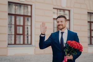 stilig ung man i kostym med bukett rosor som hälsar sin affärspartner med bukett röda rosor foto