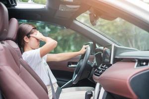 kvinna känner stress och arg under kör bil lång tid. asiatisk tjej trött och trötthet med huvudvärk sluta efter att ha kört bil i trafikstockning. sömnig, stretching och berusad koncept foto