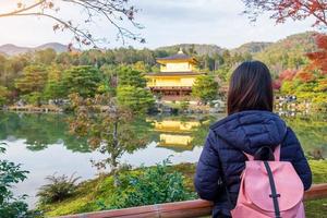 solo kvinna turist trveling på kinkakuji templet eller den gyllene paviljongen under höstsäsongen, asiatiska resenären besöker i Kyoto, Japan. semester, destination och resekoncept foto