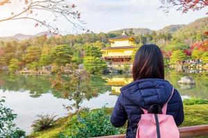 solo kvinna turist trveling på kinkakuji templet eller den gyllene paviljongen under höstsäsongen, asiatiska resenären besöker i Kyoto, Japan. semester, destination och resekoncept foto