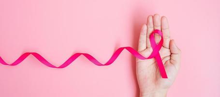 oktober bröstcancer medvetenhet månad, vuxen kvinna hand som håller rosa band på rosa bakgrund för att stödja människor som lever och sjukdom. internationella kvinnor, mor och världen cancer dag koncept foto