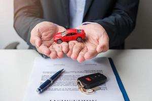 affärsman hand som håller röd bil leksak med fordon nyckellöst, penna och kontraktsdokument. köp och försäljning, försäkringar, hyres- och avtalskoncept foto
