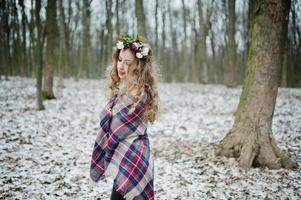 lockigt söt blond flicka med krans i rutig pläd vid snöig skog i vinterdag. foto