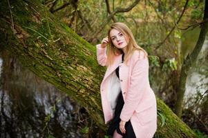 ung blond flicka på rosa kappa poserade på hösten park. foto