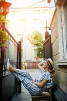 porträtt av en fantastisk ung kvinna i randig overall och hatt som sitter och poserar på stolen utomhus. foto