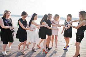 grupp av 8 tjejer bär på svart och 2 brudar på möhippo mot solig strand dricker champagne. foto