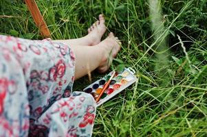 närbild av kvinnliga ben på det höga gräset tillsammans med akvarellpalett. foto