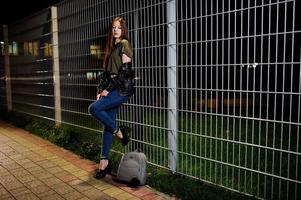 nattporträtt av flicka modell slitage på jeans och skinnjacka mot järn staket. foto